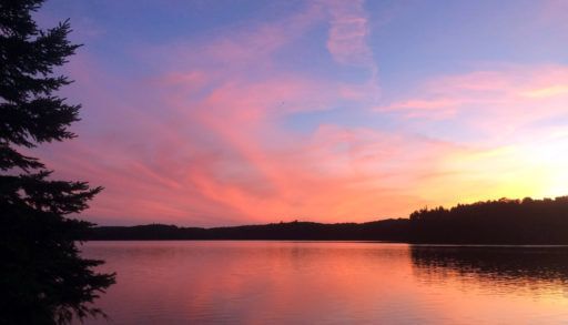 a west-facing view of a camp site on a lake at sunset.