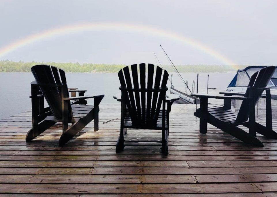 A rainbow and Muskoka chairs on a dock on Go Home Lake