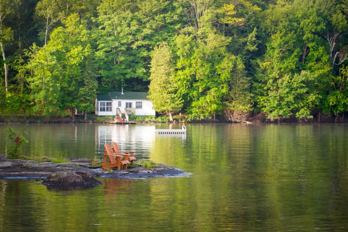 two-muskoka-chairs-across-the-lake-from-a-cottage