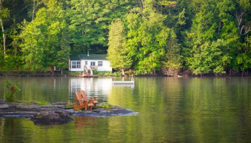two-muskoka-chairs-across-the-lake-from-a-cottage