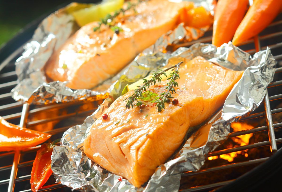 Fresh succulent salmon steaks flavoured with sprigs of thyme grilling on aluminum foil on a barbecue grill