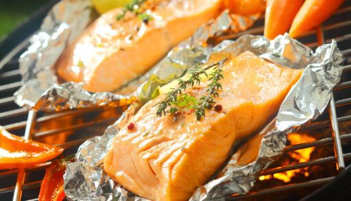 Fresh succulent salmon steaks flavoured with sprigs of thyme grilling on aluminum foil on a barbecue grill