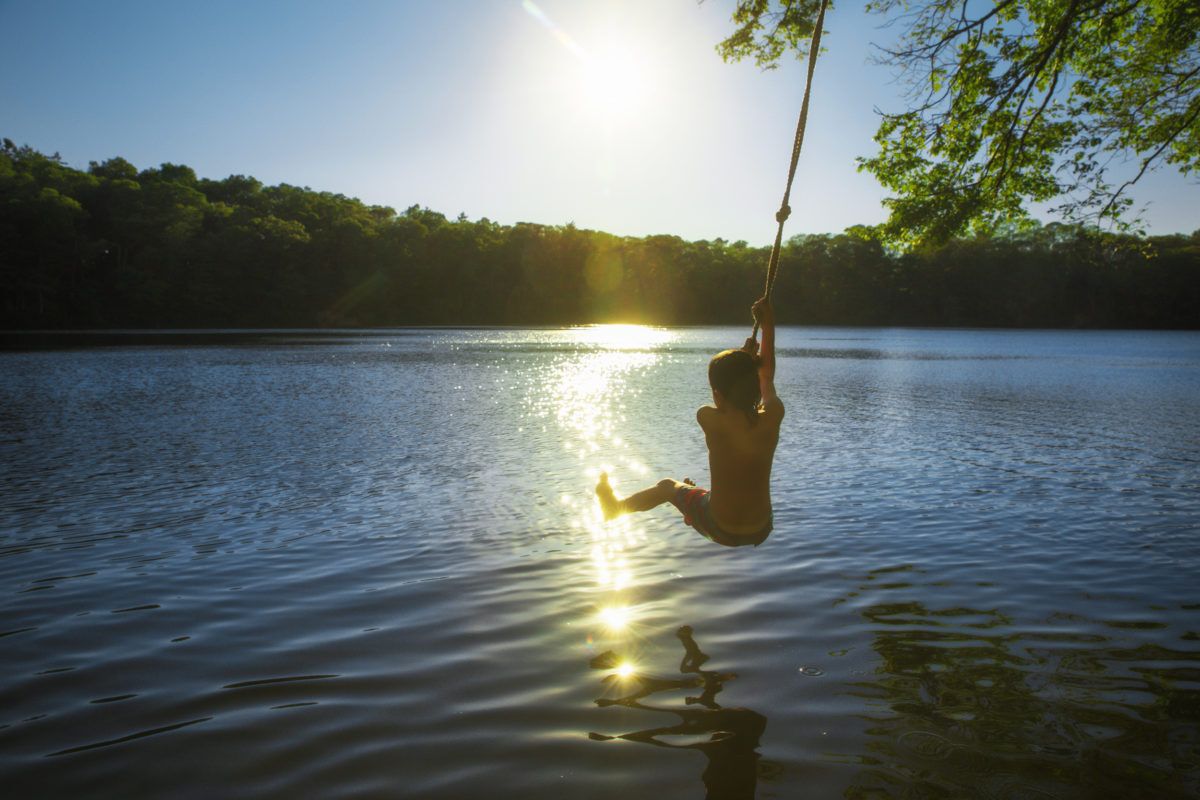boy-swinging-on-rope-swing-over-lake