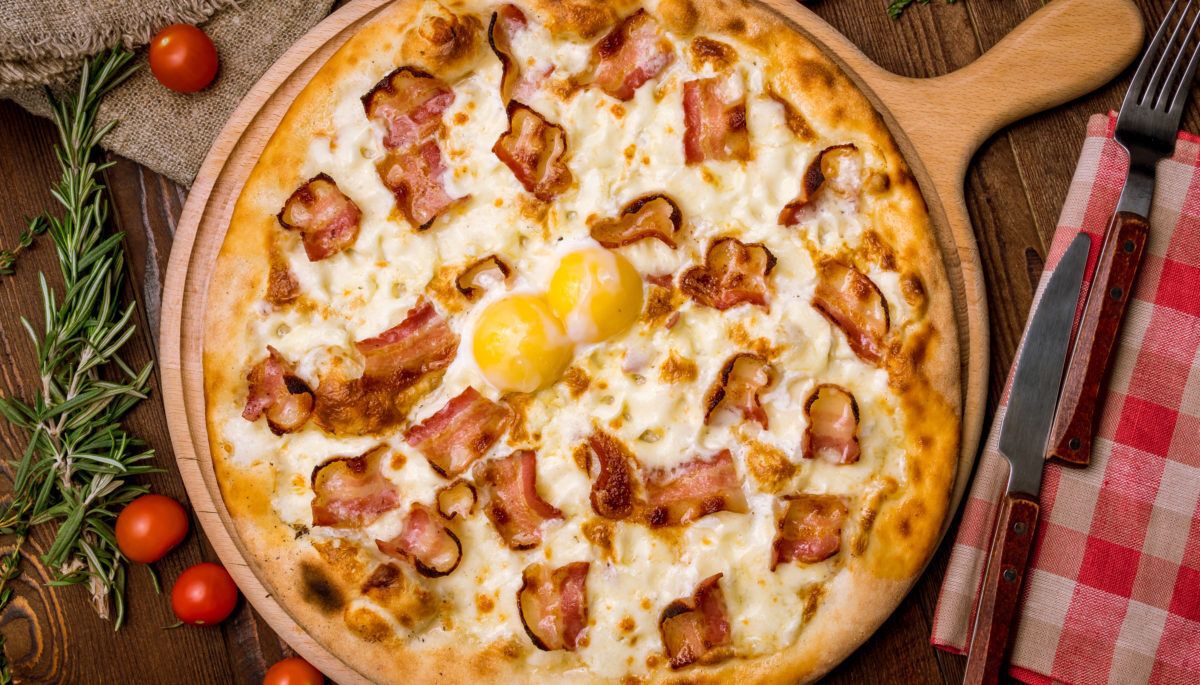 Pizza with bacon and egg with gingham napkin, thyme sprigs, and cherry tomatoes