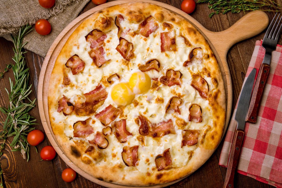Pizza with bacon and egg with gingham napkin, thyme sprigs, and cherry tomatoes