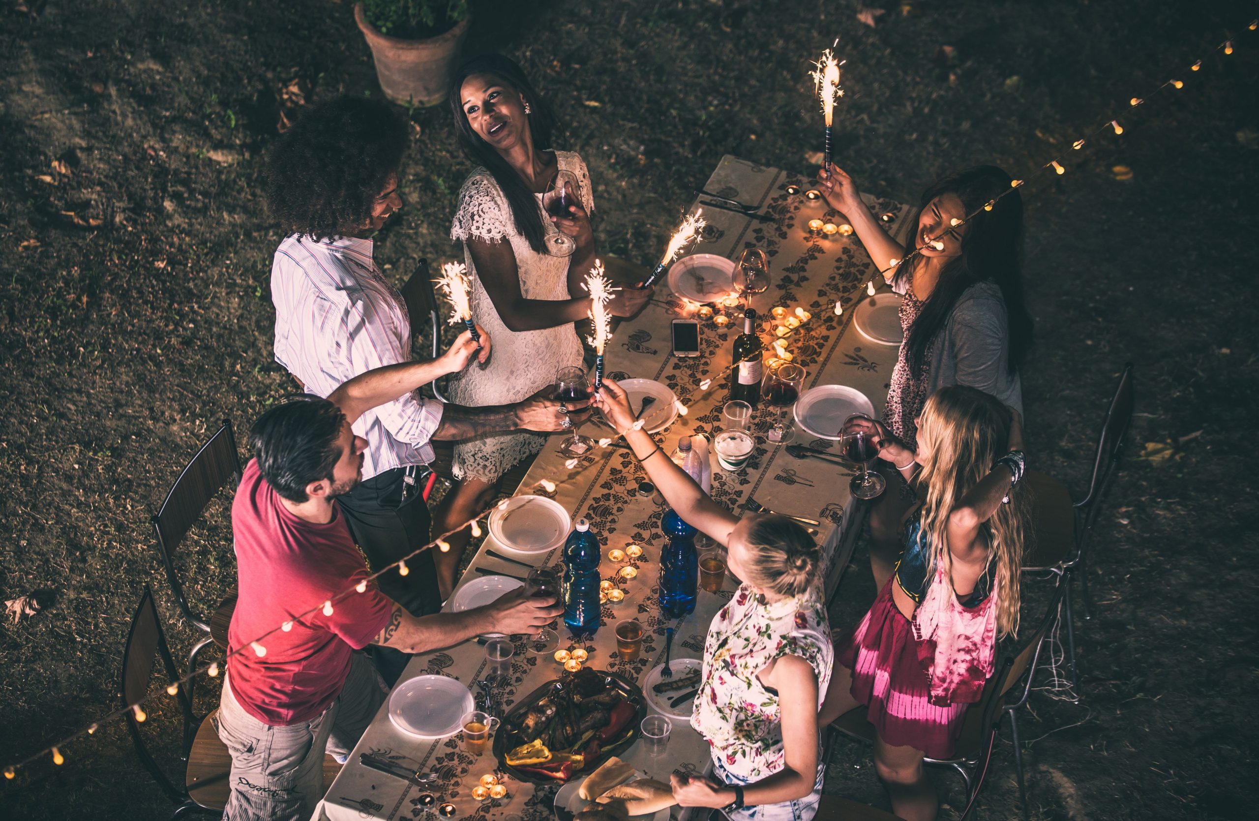 Friends gathered around an outdoor dining table, illuminated by fairy lights