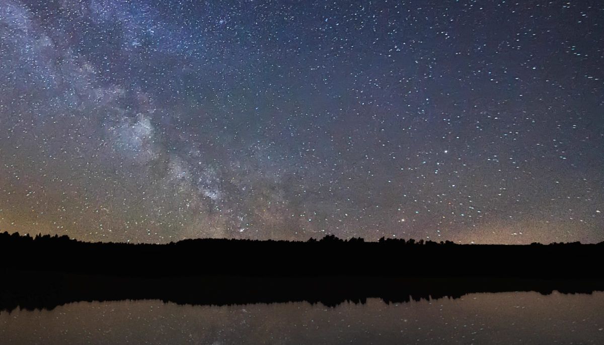 a starry sky in the country with a lake and trees