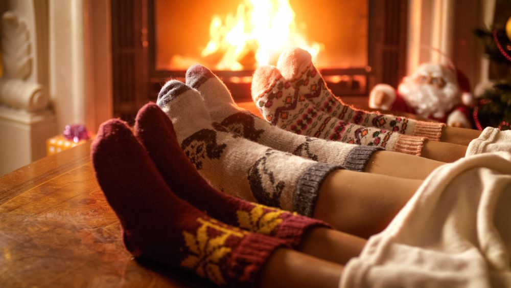 three feet wearing woolen socks in front of a fireplace