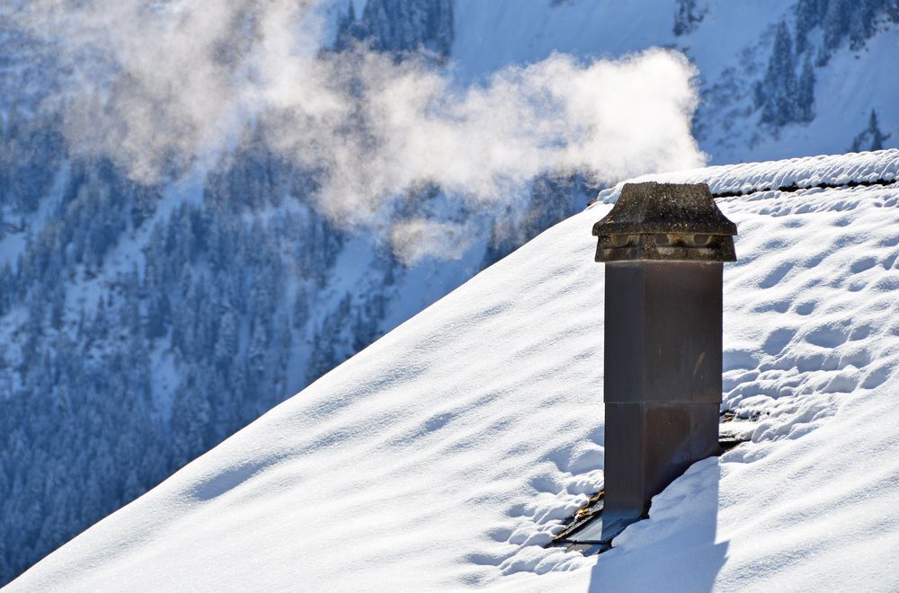 A chimney smokes on a snow-covered roof