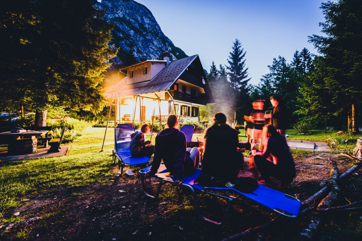 A family gathered around a campfire with a cottage in the background.