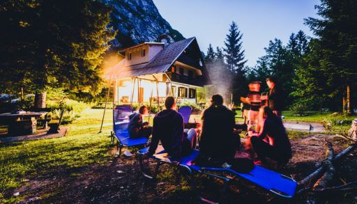 A family gathered around a campfire with a cottage in the background.