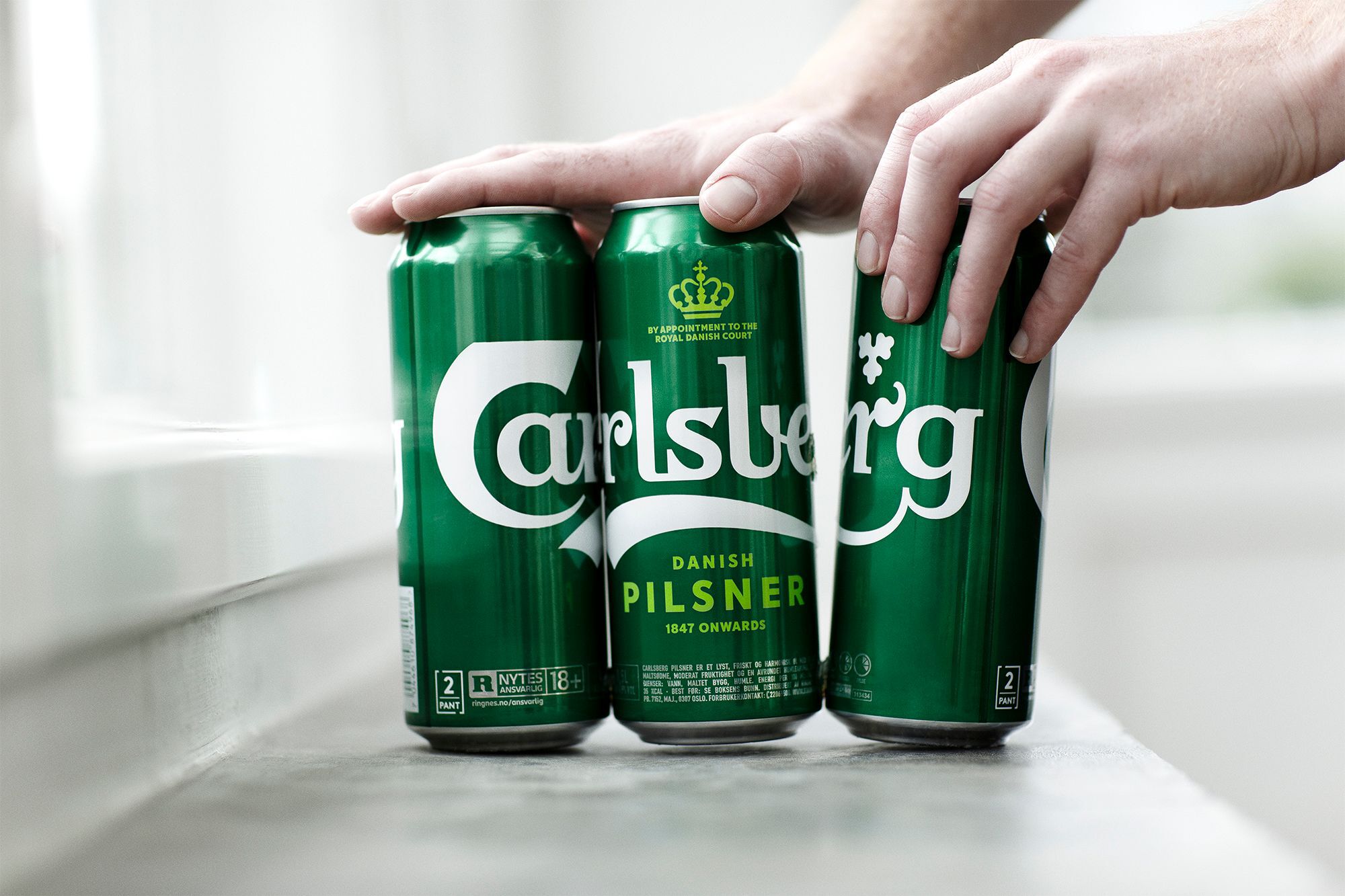 A hand reaches down to take a Carlsberg beer can out of a six-pack
