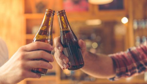 two men talking and clanging bottles of beer together