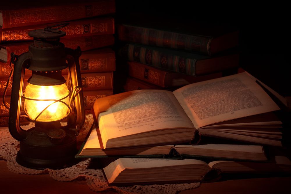 A pile of books sits by an oil lamp