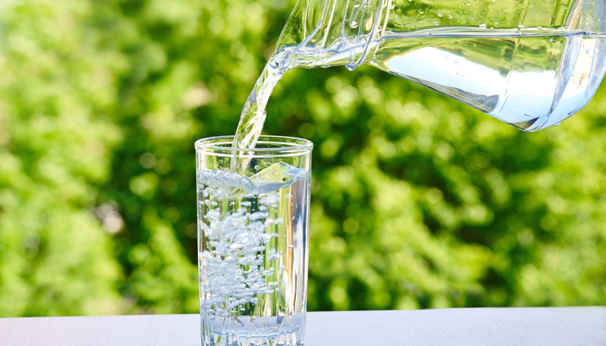 water-is-poured-from-a-jug-into-a-glass-on-a-green-nature-outdoors-background