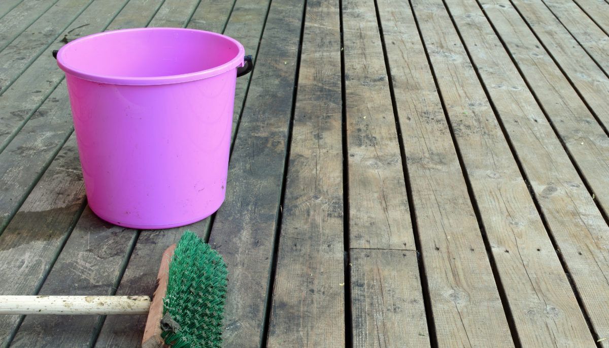 A pink bucket and a scrub brush on a dirty wooden deck.