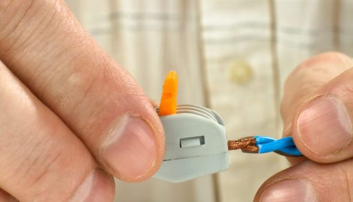 man connects the twisted-together ends of wires using compact splicing connector, closeup