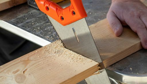 Carpenter hand with handsaw cutting wooden boards