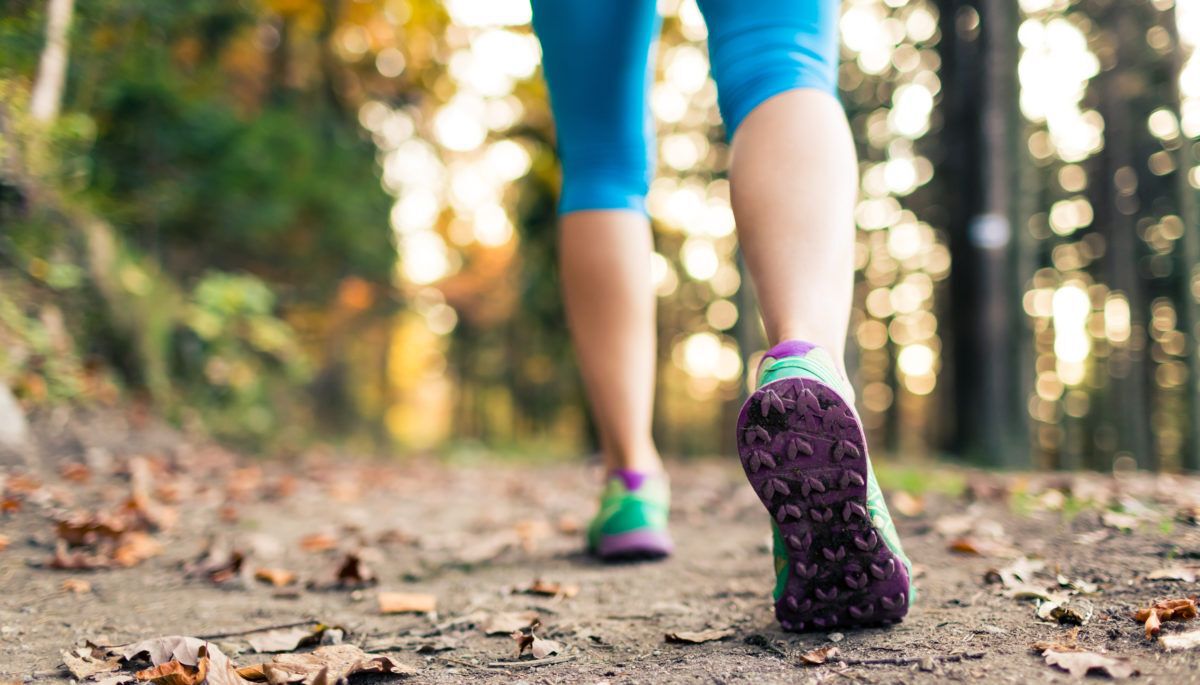 Woman's legs walking away from camera on trail in forest