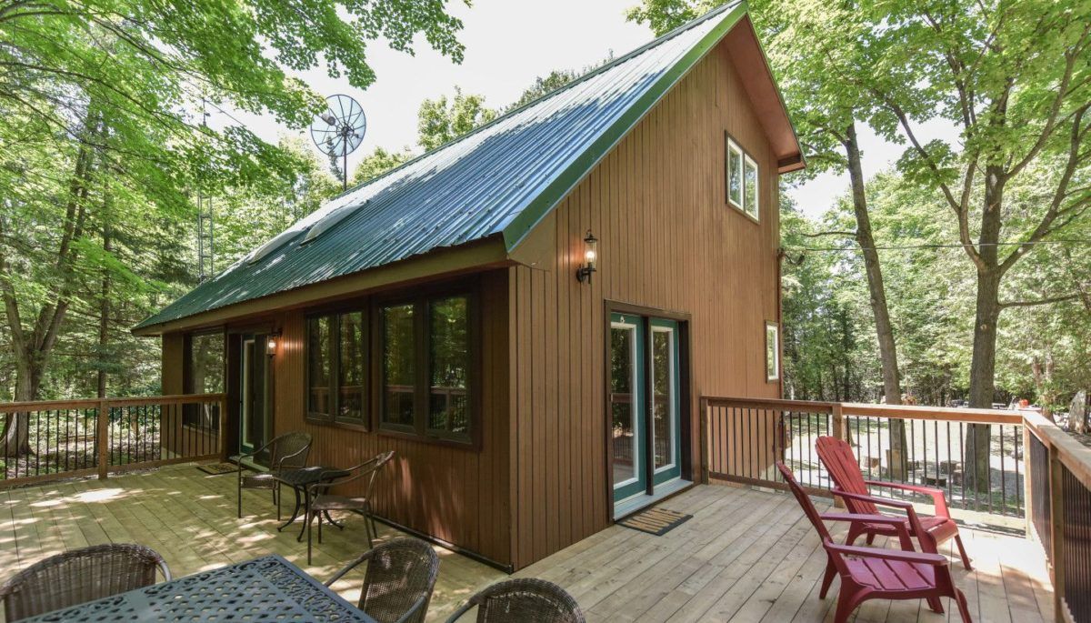 Corner view of deck and dark brown wooden cottage with green roofing