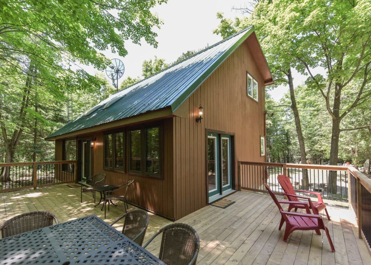 Corner view of deck and dark brown wooden cottage with green roofing