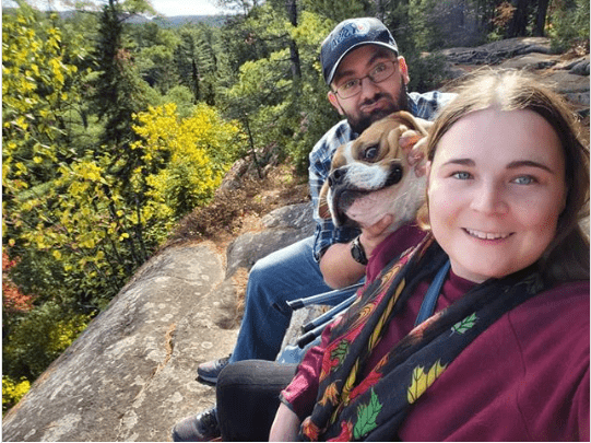 funny animal photo, dog with goofy grin next to owners on a hike