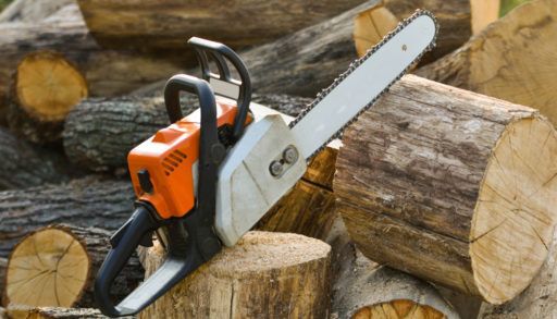 Chainsaw that stands on a heap of firewood in the yard on a beautiful background of green grass and forest