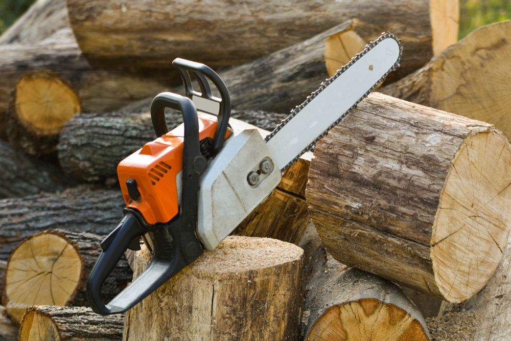 Chainsaw that stands on a heap of firewood in the yard on a beautiful background of green grass and forest