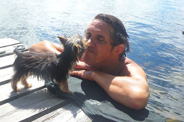 tiny puppy kissing man swimming in a lake, love