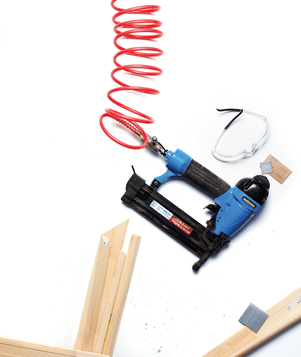 nail gun on white surrounded by safety glasses and pieces of wood trim