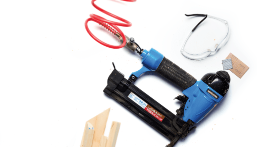 nail gun on white surrounded by safety glasses and pieces of wood trim