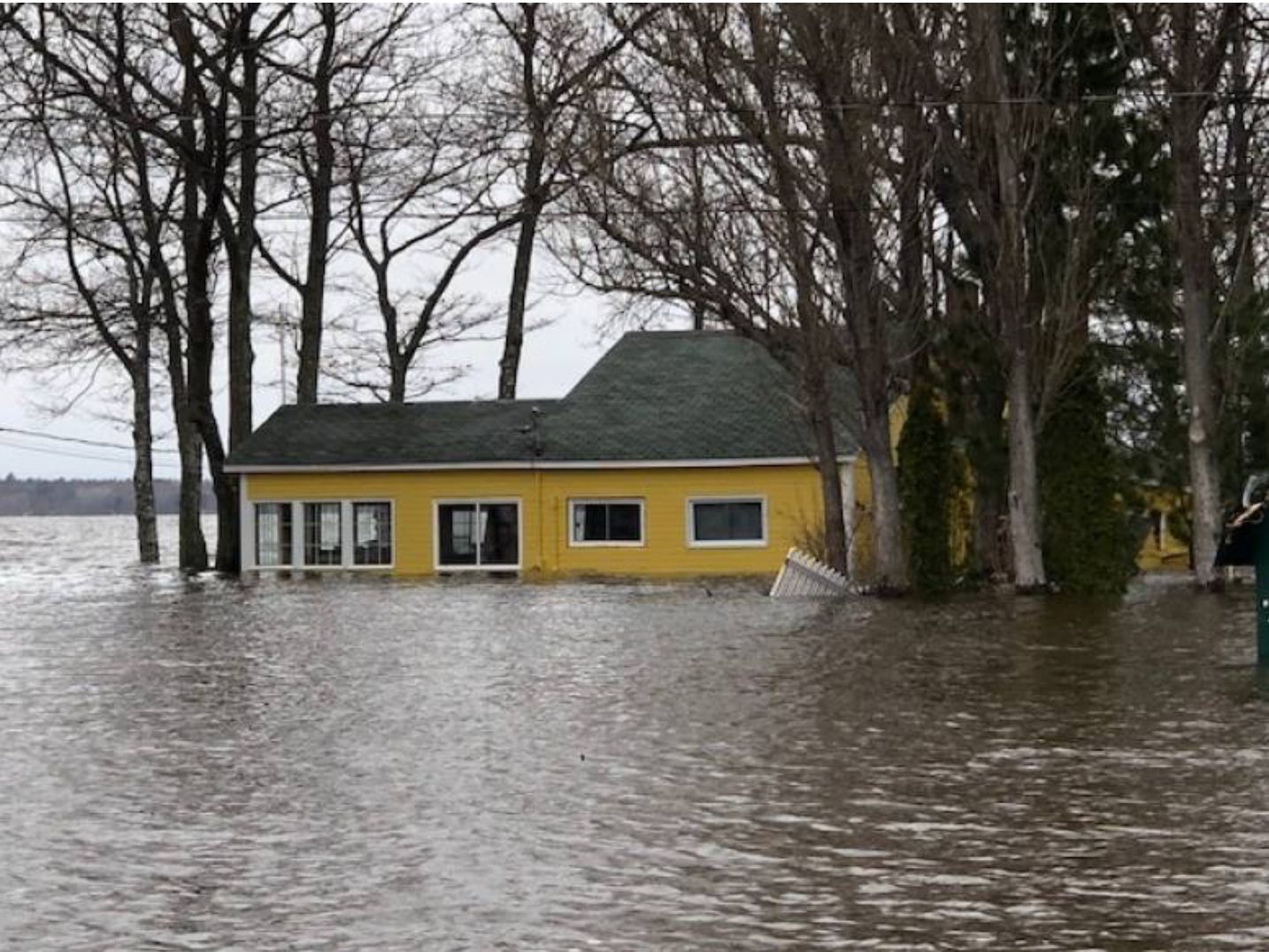 A yellow cottage is half-submerged in floodwaters