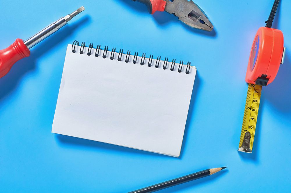 Different tools lies near blank paper notebook on blue desk in workshop, chores
