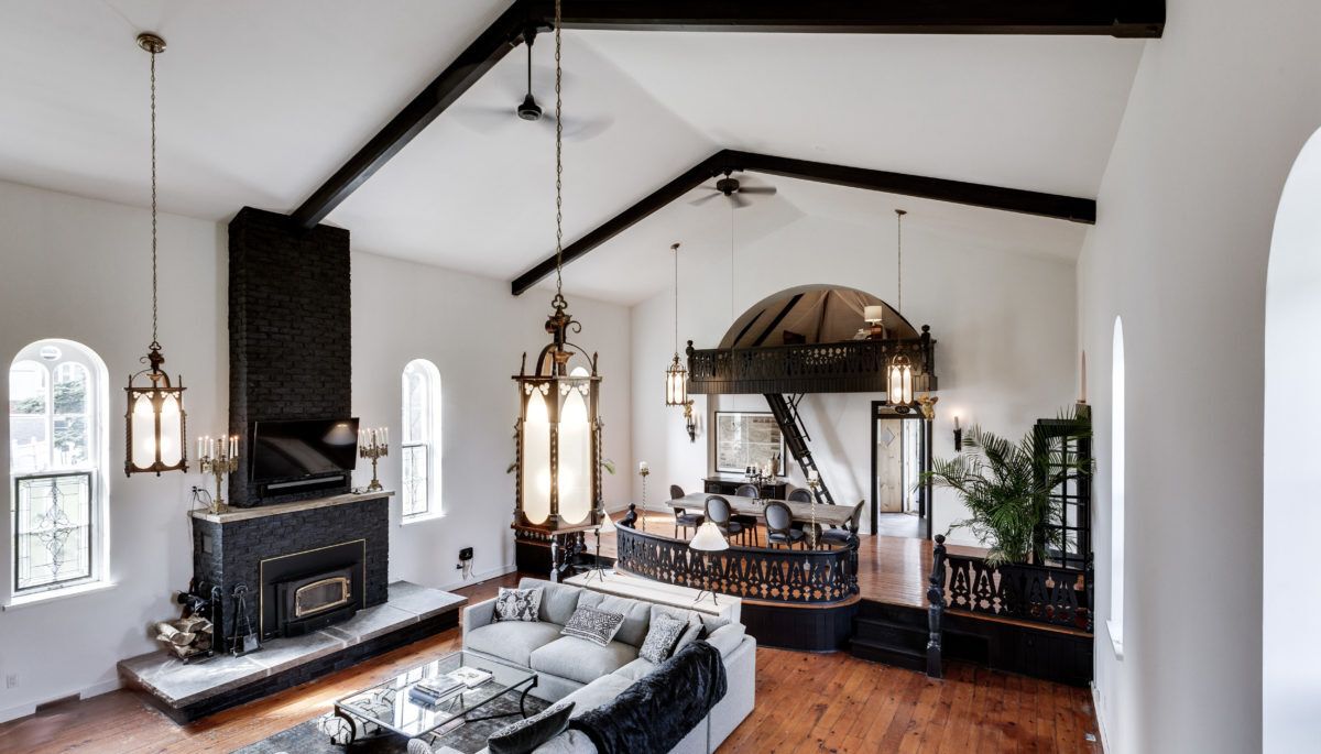 Main room of converted church with soaring ceilings , massive sectional couch and wood burning fireplace