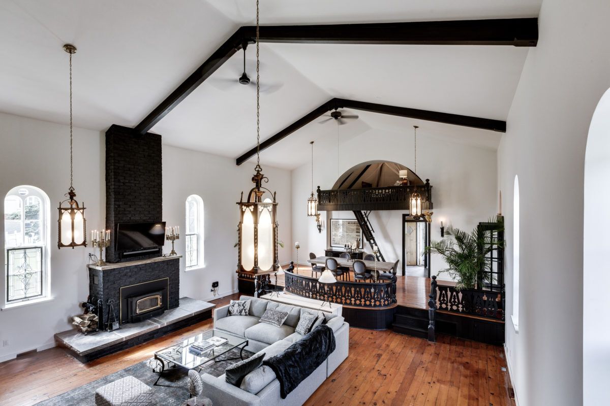Main room of converted church with soaring ceilings , massive sectional couch and wood burning fireplace