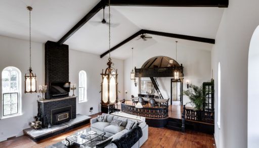 Main room of converted church with soaring ceilings , massive sectional couch and wood burning fireplace