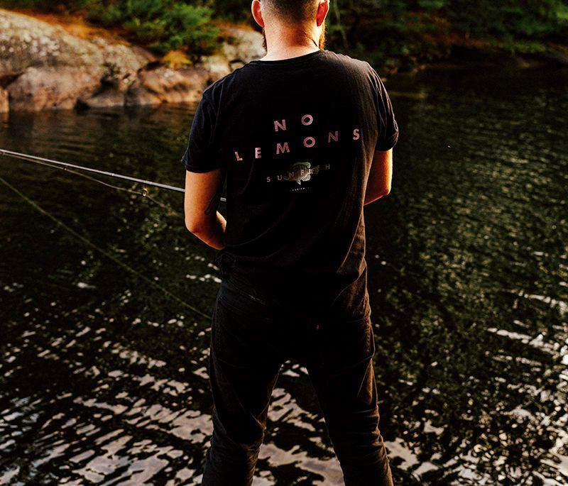 Derek Blais standing on Georgian Bay rock fishing with a black no lemons shirt