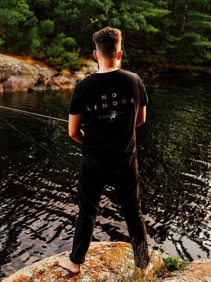 Derek Blais standing on Georgian Bay rock fishing with a black no lemons shirt