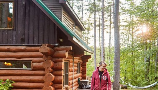 Stephen Gardner outside his log cabin with kids running around
