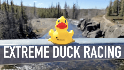 Yellow rubber duck sitting on railing over river with text "Extreme Duck Racing" under it.