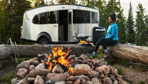 woman sitting around a campfire outdoors in front of an Airstream RV