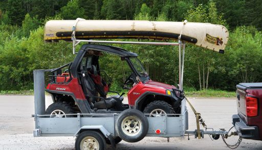 small utility vehicle on a small utility trailer with a canoe on top attached to a truck