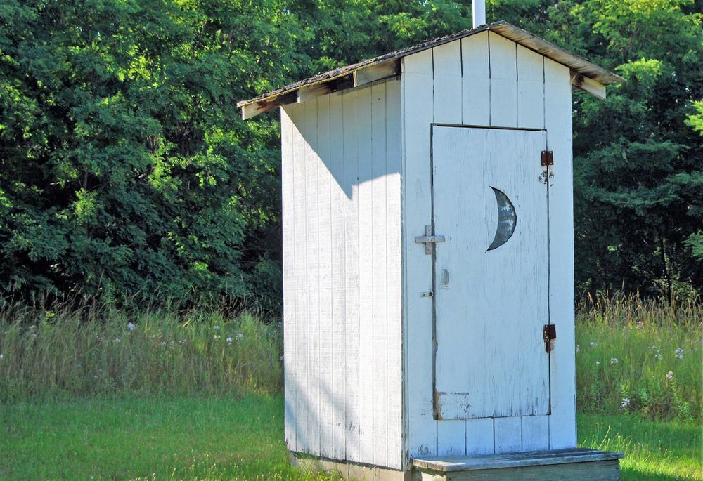 A white outhouse in a field