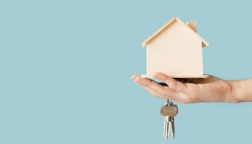 Close-up of young hand holding keys and wooden house model against blue background