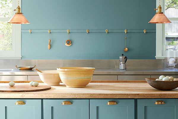 teal colour wall and cabinets in a kitchen with a light wood countertop and gold accents