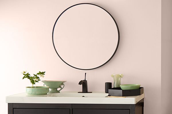 bathroom with a round mirror on the wall, a subtle pink paint colour, dark cabinet and light countertop