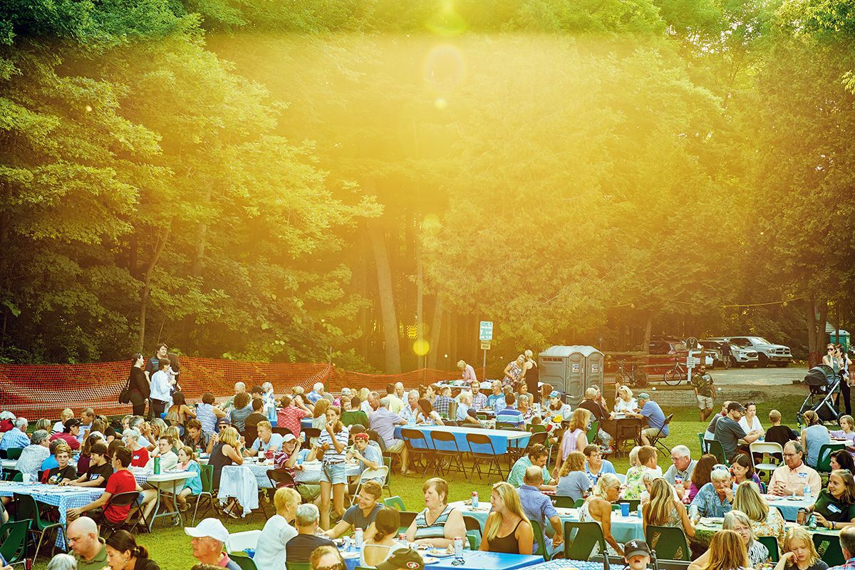 big group of people sitting at set up tables in a field, annual bruce beach picnic