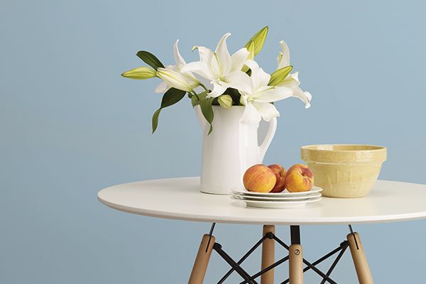 light blue paint colour on a wall behind a white table with a white vase with white flowers and peaches on a plate