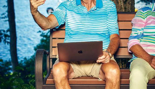 older man holding up a cell phone and a laptop trying to communicate