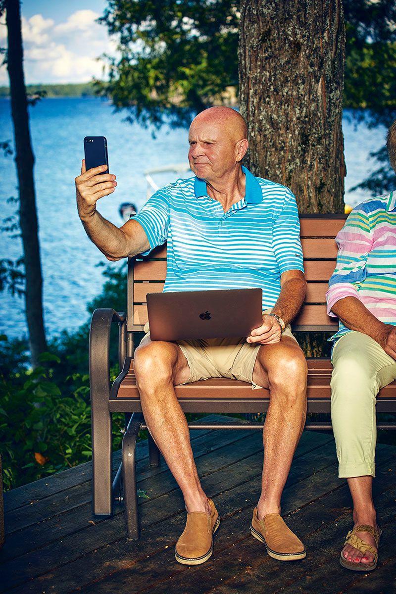older man holding up a cell phone and a laptop trying to communicate